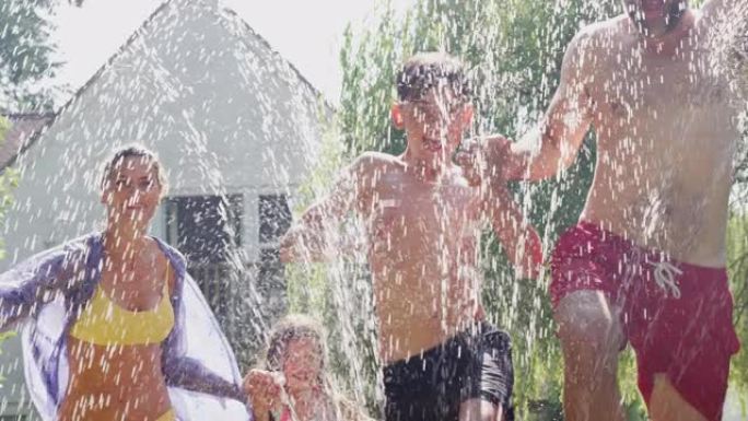 一家人从花园洒水装置中穿水，穿着游泳衣玩得开心