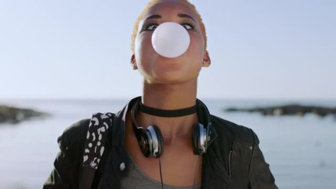 年轻的黑人妇女，脸和泡泡糖户外海滩，旅行和度假在亚特兰大。在海洋上嚼口香糖泡泡、糖果和糖果，带着顽皮