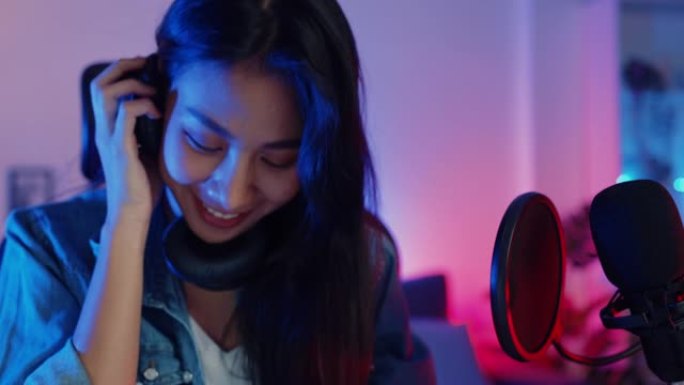 快乐亚洲女孩dj播放启动板合成器键盘混音器戴着耳机和表演音乐在线直播晚上在客厅家庭工作室与观众交谈。