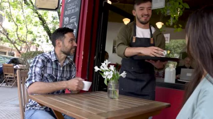 友好的服务员在外面的一家咖啡馆为幸福的夫妇提供咖啡和小吃
