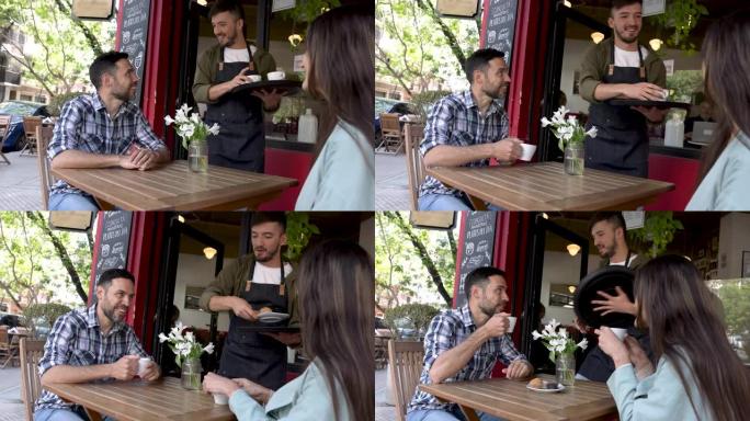 友好的服务员在外面的一家咖啡馆为幸福的夫妇提供咖啡和小吃