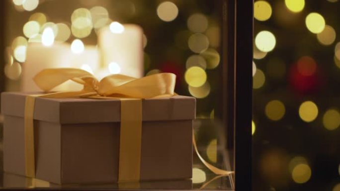 圣诞老人的手的特写镜头，将礼品盒放在架子上，背景是圣诞树