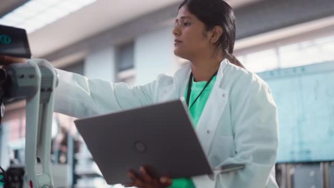 年轻的印度女工程师在工厂开发车间测试工业可编程机器人动物。专业研究人员在实验室外套中使用笔记本电脑开