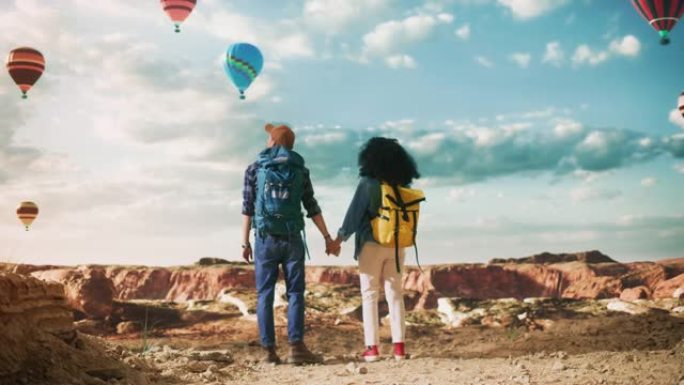 年轻的多样化旅游夫妇带着背包在落基峡谷谷的大荒野徒步旅行。男女牵手冒险之旅。山区国家公园的热气球节。