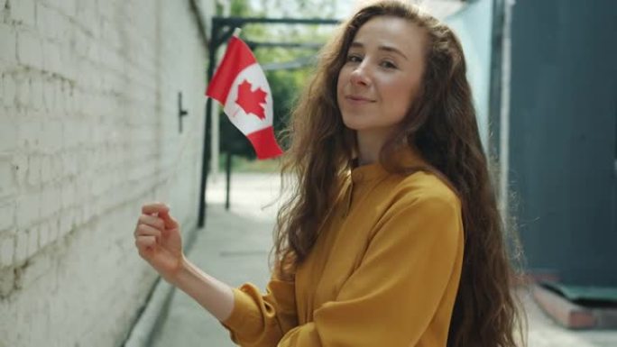 快乐的年轻女士的肖像挥舞着加拿大国旗，微笑着站在城市的户外