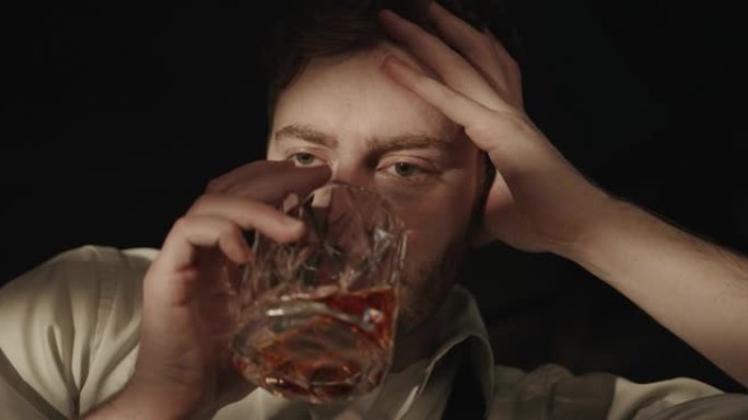 一个绝望的醉汉的特写镜头，他坐在黑暗的房间里喝威士忌，因为他遇到的问题而受苦