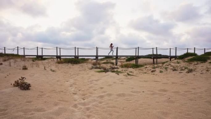 在海滩上的木板路上奔跑的无法识别的女运动员的广角倾斜镜头