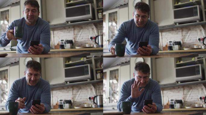 微笑的白人男子使用智能手机，在家中厨房里喝咖啡