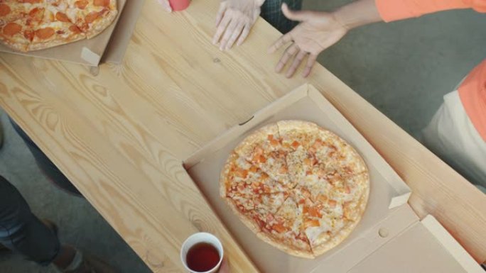 在办公室的木桌上，男性手提披萨和打开纸板箱的特写镜头