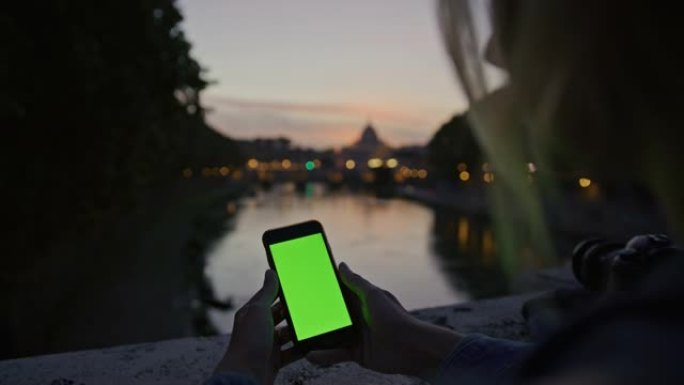 黄昏时，SLO MO女人在桥圣安吉洛对面的桥上使用带有色键显示的智能手机
