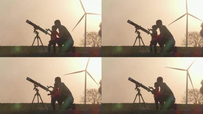 家庭和父亲的剪影日落教学给2岁的男婴使用望远镜一起观察行星和星系，而风力涡轮机回到背景。教孩子们关于