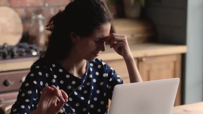 在笔记本电脑上工作的女人摘下眼镜以减轻眼睛疲劳