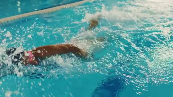 美丽的女游泳者使用前爬行，在游泳池自由泳。立志夺冠的职业运动员。电影慢动作，时尚色彩，艺术跟踪镜头