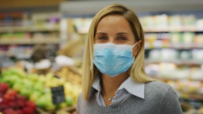 戴着医用口罩以保护自己免受疾病侵害的年轻女子的真实照片在超市里买杂货时，用购物车带着精选的食品在相机