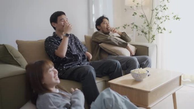快乐的亚洲男人手臂残疾和朋友在家里看喜剧电影，在地板上吃爆米花。