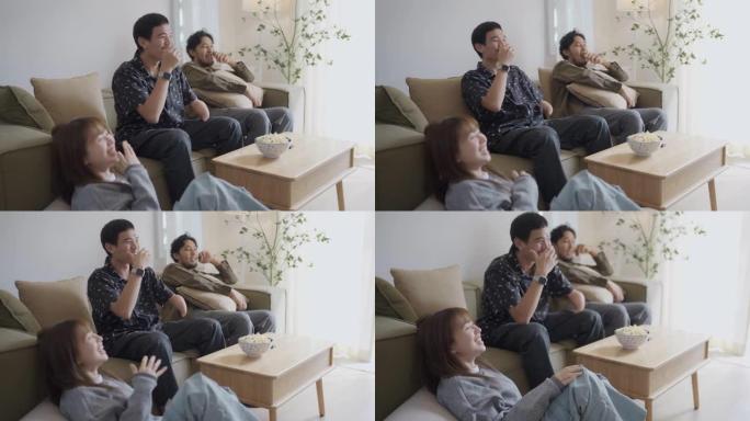 快乐的亚洲男人手臂残疾和朋友在家里看喜剧电影，在地板上吃爆米花。