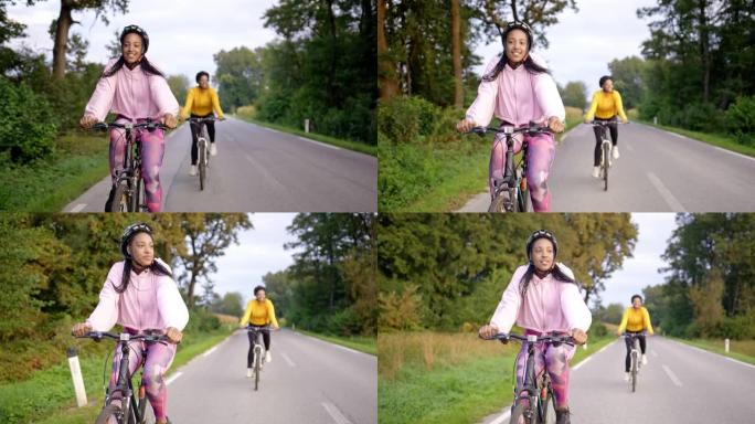 跟踪两名成年成年女性的手持照片，在经过森林的高速公路上骑自行车，慢动作