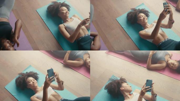 4k视频片段，一名年轻女子在与朋友一起上瑜伽课时使用智能手机
