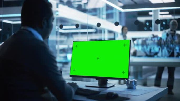 软件开发人员在绿屏模拟显示的计算机上工作。科学实验室，工程研究中心，后台有从事涡轮发动机开发的专家。