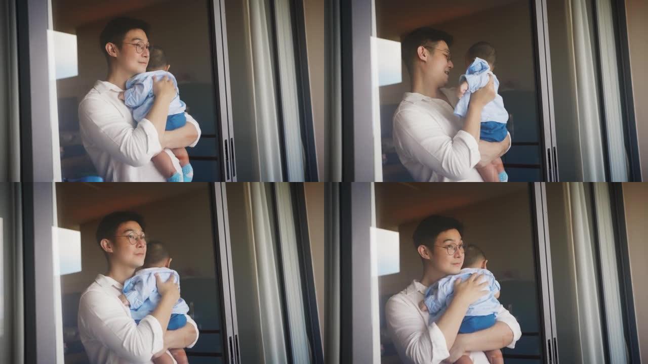 父亲抱着并亲吻可爱的新生男婴，看着窗外。单身父母，真实的生活方式育儿父亲时刻