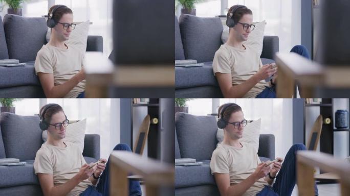 4k视频片段，一个年轻人坐在客厅地板上，戴着耳机使用手机
