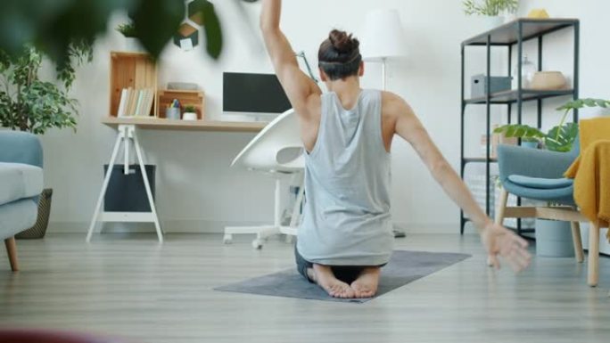 肌肉发达的年轻人伸展手臂坐在瑜伽垫上独自在家锻炼