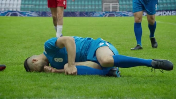 职业足球足球比赛冠军: 蓝队球员进攻，输球犯规。国际锦标赛上的动作游戏。慢动作运动员跌倒后躺在草地上