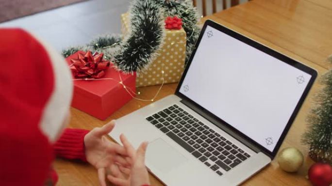 戴着圣诞老人帽子的白人妇女在笔记本电脑上在家进行视频通话，屏幕上有复制空间