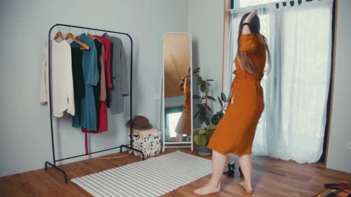 享受新衣服。年轻迷人兴奋的高加索博客女人在镜子前跳舞，穿着芥末连衣裙感觉很棒。