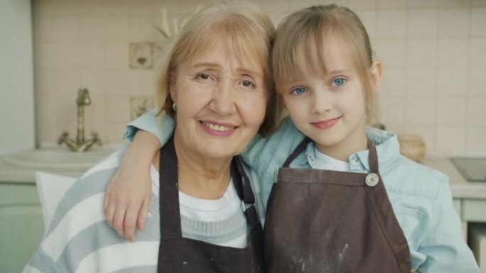穿着围裙的祖母和孙女的肖像在厨房里看着相机
