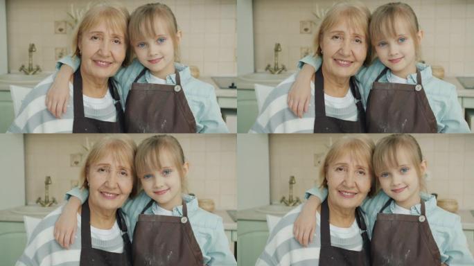 穿着围裙的祖母和孙女的肖像在厨房里看着相机