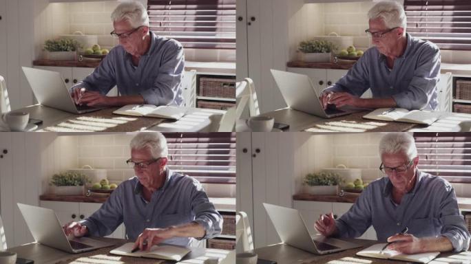 4k视频片段，一名高级男子独自坐在家里的厨房里，使用笔记本电脑