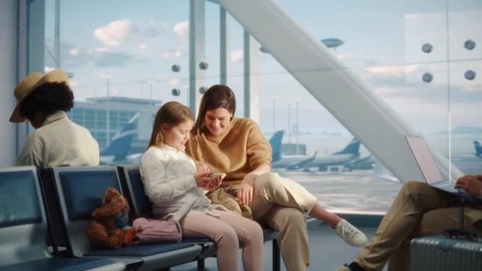 繁忙的机场飞机航站楼: 快乐美丽的母亲和可爱的小女儿等待他们的假期航班，使用移动智能手机娱乐。航空枢