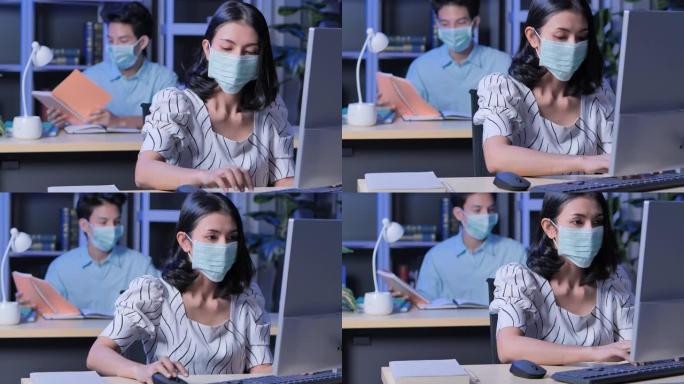 新型冠状病毒肺炎大流行后，在办公室里戴着电脑的亚洲女商人戴着口罩，而同事在晚上工作到很晚。在 “新”