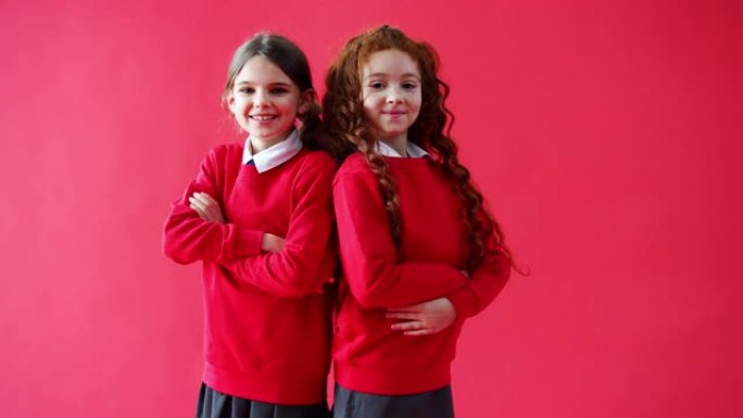 两名在红色工作室背景下背靠背穿着制服的女小学生