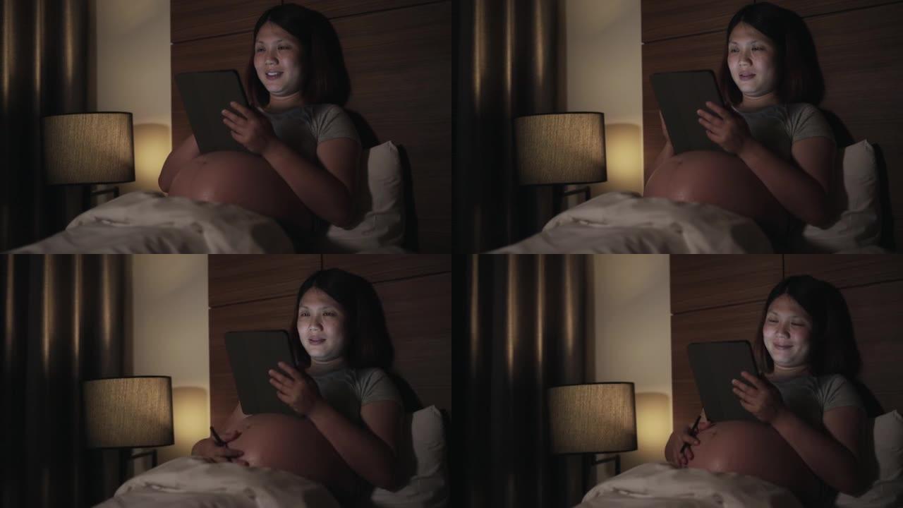 孕妇在卧室晚上使用数字平板电脑加班