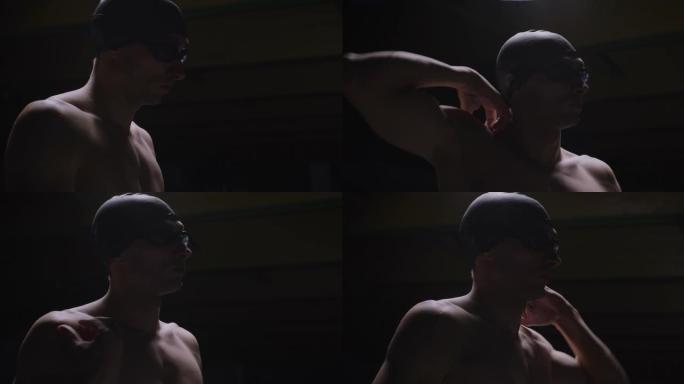 年轻的职业男游泳者带帽的电影镜头正在进行热身运动，并在游泳池训练前戴上护目镜。运动、竞争、胜利、健身