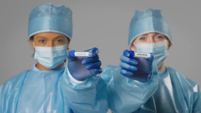 工作室拍摄的照片中，女性实验室研究人员穿着个人防护用品，手持标有Covid-19和欧米克隆的试管