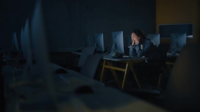 紧张的男学生独自坐在大学信息学室，晚上在计算机科学项目上工作。累了的学者在大学里用电脑研究它，写作业