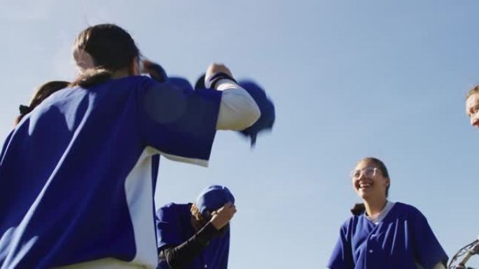 快乐的多元化女子棒球运动员队伍向空中投掷帽子，庆祝赛后