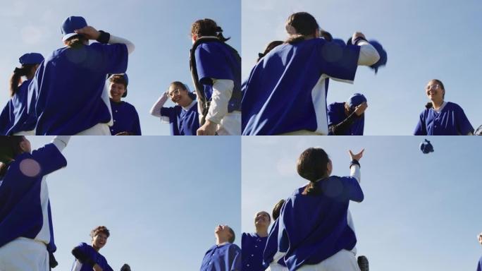 快乐的多元化女子棒球运动员队伍向空中投掷帽子，庆祝赛后