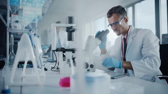 医学发展实验室: 白人男性科学家在显微镜下观察，将数据输入数字平板电脑。高级制药实验室从事医学、生物