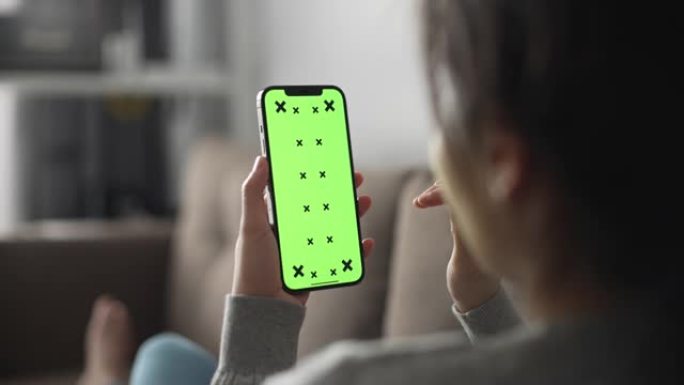 年轻女子在家中使用带有绿屏的智能手机