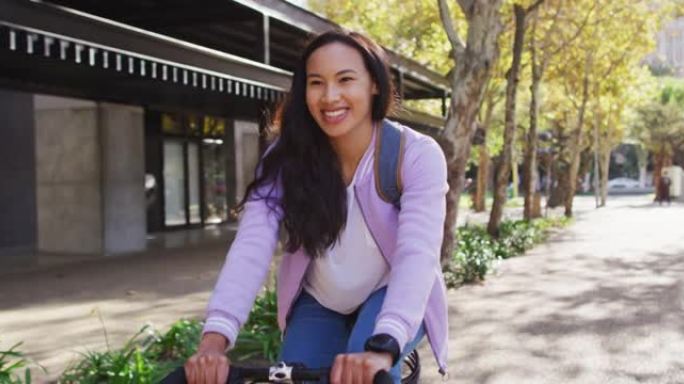 穿着背包的亚洲女子在路上骑自行车微笑