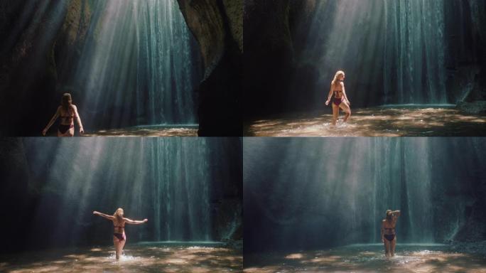 快乐的女人穿着比基尼在瀑布洞穴跳舞，享受双臂举起的自由，感觉无忧无虑的热带假期4k