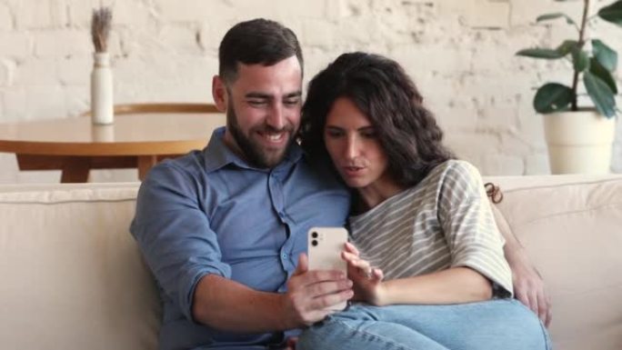 可爱的年轻夫妇在智能手机屏幕上的沙发上拥抱
