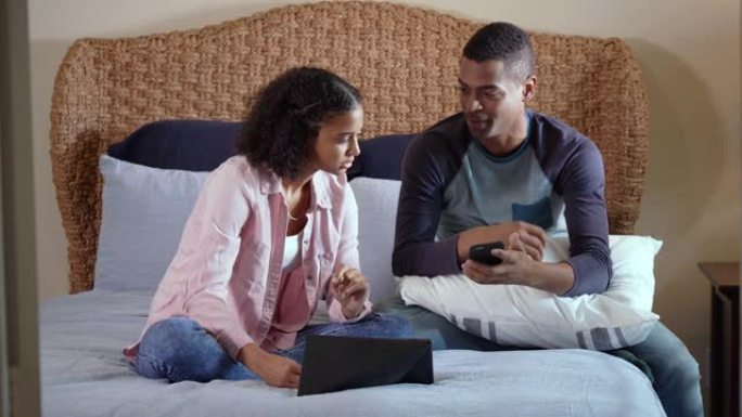 年轻的黑人夫妇坐在床上，网上比较购物