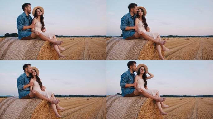 中年夫妇坐在干草捆上，拥抱并欣赏日落的手持慢动作镜头