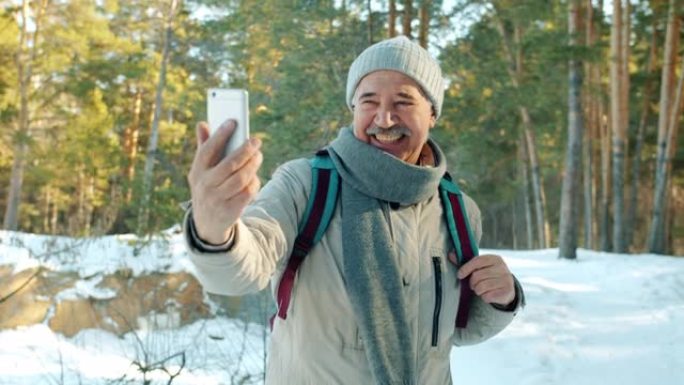 快乐的老人游客在冬季森林用智能手机进行在线视频通话