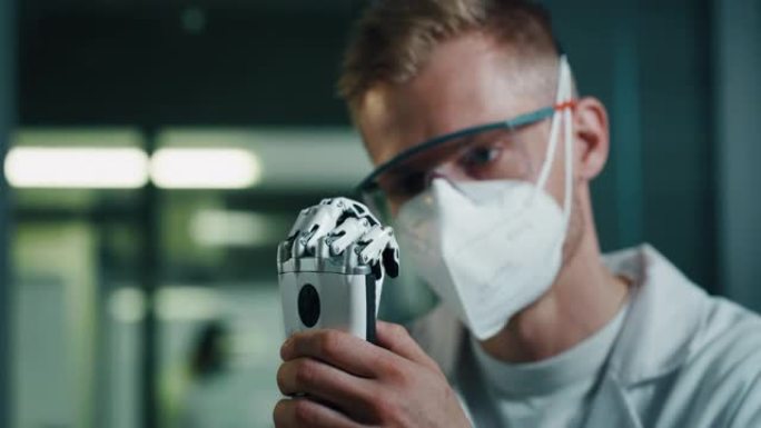 年轻工程师用螺丝刀调整现代仿生肢体的特写。在为残疾人制作高级机器人手掌时，戴着防护口罩和眼镜的人。